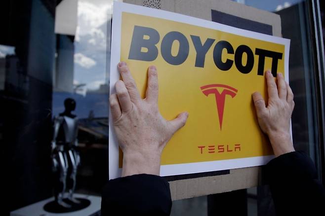 지난 1일 미국 뉴욕의 한 테슬라 매장 앞에서 일론 머스크를 반대하는 시위대가 '테슬라 불매' 전단지를 붙이고 있다. /AFP