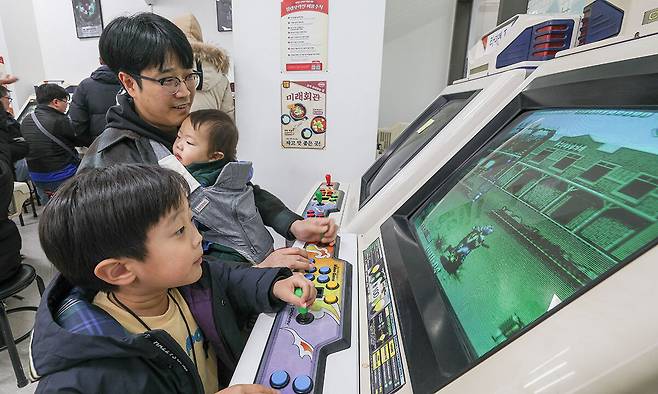 서울 동대문구 청량오락실에서 한 아버지가 막내를 안은 채 아들과 함께 카발 2 블러드 브라더스 게임을 즐기고 있다.