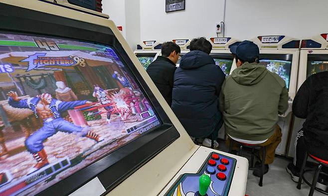 서울 동대문구 청량오락실에 더 킹 오브 파이터즈 98 오락기가 구동되고 있다. 그 뒤로 시민 셋이 던전앤드래곤2를 같이 즐기고 있다.