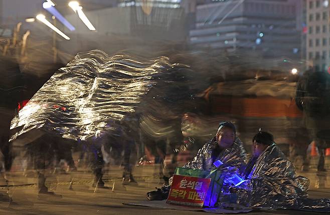 경기도 하남시에서 초등학교 5학년생 아들 최아진군과 함께 온 박상민씨가 은박지로 몸을 두른 채 민주노총 주최로 열린 ‘윤석열 석방 규탄, 헌재 파면 촉구 비상 결의대회’를 지켜보고 있다.