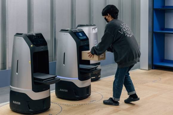 네이버 직원이 1784 사옥에서 로봇 ‘루키’가 배달한 택배 물품을 받고 있다. 네이버 1784 사옥에서는 100여대의 로봇이 간단한 심부름을 수행하는데 이는 건물 인프라와 네이버클라우드, 5G 네트워크가 통합된 ‘ARC’(AI·Robot·Cloud) 시스템으로 운용된다. 네이버 제공
