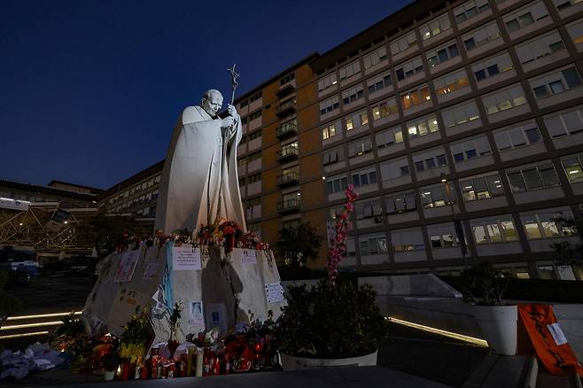 프란치스코 교황이 입원해 있는 이탈리아 로마 소재 병원 앞 교황 요한 바오로 2세 동상에 시민들이 18일(현지시간) 교황의 건강 회복을 기원하며 꽃과 메시지를 남기고 있다. [EPA]
