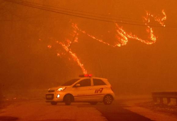 화마가 남부 지역을 나흘째 덮친 가운데 25일 경북 안동시 길안면 백자리에서 소방 관계자들이 대피 명령이 내려진 마을을 통제하고 있다. 사진 위쪽으로는 산이 화염에 휩싸여 있다. 유네스코 세계문화유산인 하회마을과 병산서원이 있는 안동에서는 전 시민 대피령이 내려졌다. ﻿  안동 뉴스1