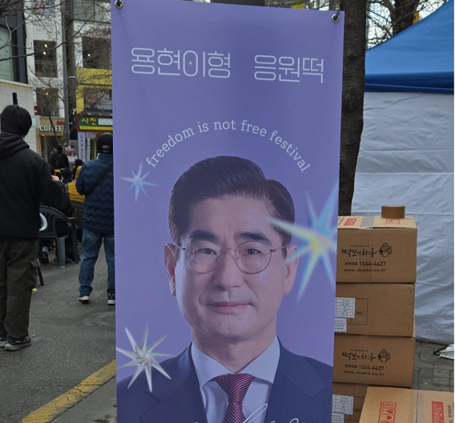 29일 서울 서대문구 신촌역 일대에서 '탄핵을 반대하는 대한민국 청년' 등 주최로 열린 자유 토크쇼에 김용현 전 국방부 장관이 떡을 돌렸다는 내용을 적은 입간판이 설치돼 있다. 엑스(X) 캡처