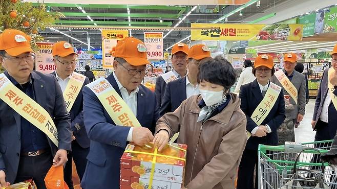 주황색 모자와 어깨띠를 두른 관계자가 직접 소비자에게 천혜향 박스를 건네주고 있다. 제주 감귤을 손에 쥔 순간, 소비자와 제주 사이의 거리는 더 이상 멀게 느껴지지 않는다. (제주농협 제공)