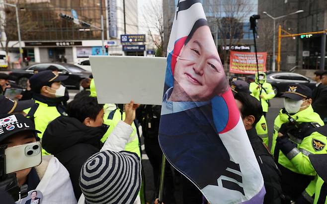 내란 우두머리 혐의로 기소된 윤석열 전 대통령의 첫 형사재판이 열린 4월14일 서울 서초구 서울중앙지방법원 앞에서 한 지지자가 윤 전 대통령 얼굴이 새겨진 태극기를 들고 서 있다. ⓒ 연합뉴스