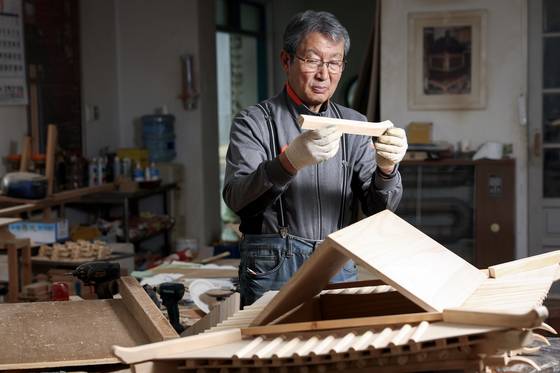 Master craftsman Lee Kang-yeon holds up a wooden piece of a palanquin at his workshop in Paju, Gyeonggi on April 2. [JUN MIN-KYU]