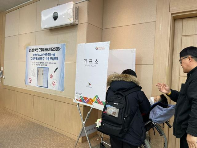 1월 9일 서울 여의도 이룸센터 내 장애인차별금지추진연대가 개최한 모의투표 행사에서 한 장애인이 투표 보조인의 도움을 받으며 투표하고 있다. 장애인차별금지추진연대 제공