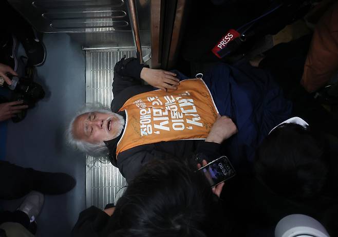 박경석 전국장애인차별철폐연대(전장연) 공동대표가 21일 서울 지하철 4호선 혜화역에서 제62차 ‘출근길 지하철 탑니다’ 시위를 벌이던 중 이를 저지하던 서울교통공사 관계자와 충돌하며 열차 입구에 넘어져 있다.[사진제공=연합뉴스]