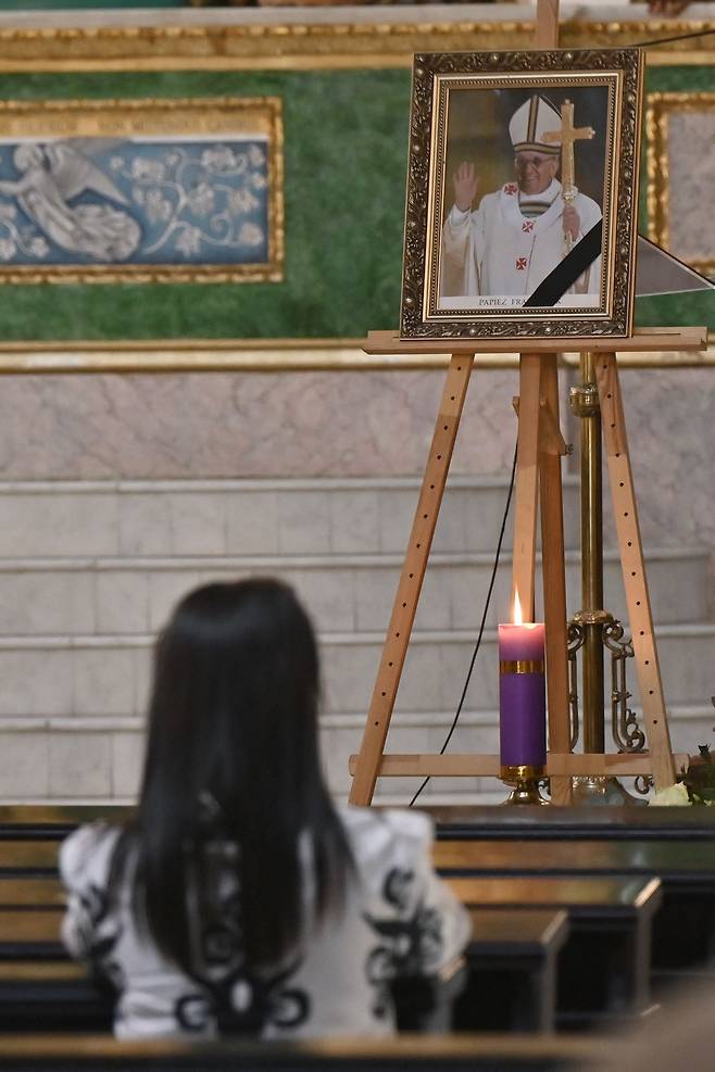 우크라이나 시민이 21일(현지시간) 키이우 성 알렉산더 대성당의 프란치스코 교황 초상화 앞에서 경의를 표하고 있다. AFP연합뉴스