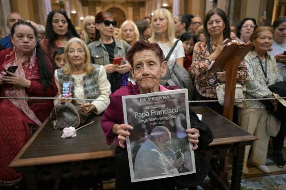 프란치스코 교황 선종 이튿날인 22일(현지시간) 한 여성이 부에노스아이레스 대성당에서 열린 종교 간 미사 중 고(故) 프란치스코 교황의 사진이 실린 신문 1면을 펼쳐 보이고 있다. AFP=연합뉴스