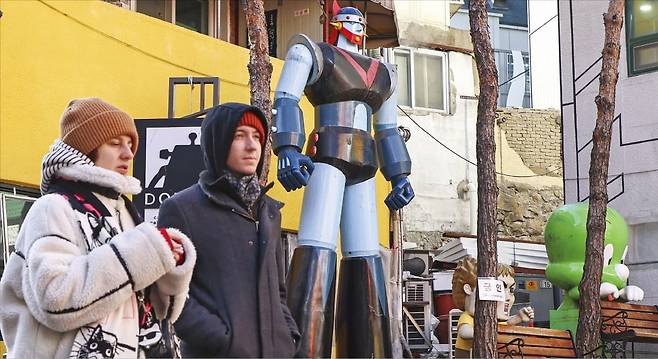 지난 2월 서울 명동 재미로(만화거리)에서 외국인들이 한국 애니메이션인 ‘로보트 태권브이’ ‘아기공룡 둘리’ 조형물 옆을 지나가는 모습.   임형택 기자