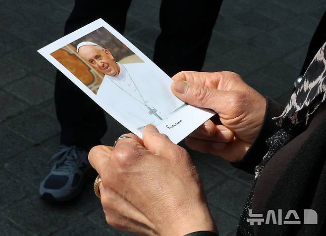 [서울=뉴시스] 이영환 기자 = 프란치스코 교황이 선종한 가운데 24일 오전 서울 중구 명동대성당 앞에서 한 천주교 신자가 프란치스코 교황 사진을 들고 있다. 2025.04.24. 20hwan@newsis.com