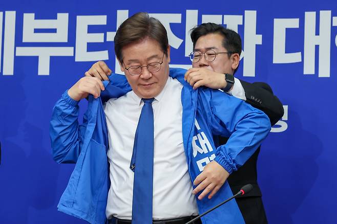 박찬대 더불어민주당 대표 직무대행 겸 원내대표가 28일 서울 여의도 국회에서 열린 최고위원회의에서 이재명 대선 후보에게 선거복을 입혀주고 있다./뉴스1