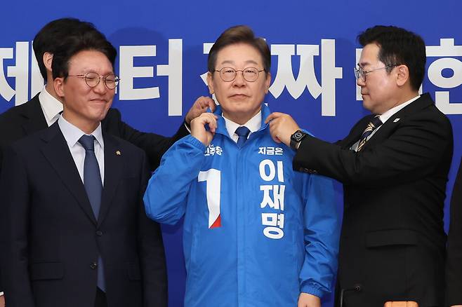 박찬대 더불어민주당 대표 직무대행 겸 원내대표가 28일 서울 여의도 국회에서 열린 최고위원회의에서 이재명 대선 후보에게 선거운동용 파란색 점퍼를 입혀주고 있다. ⓒ연합뉴스