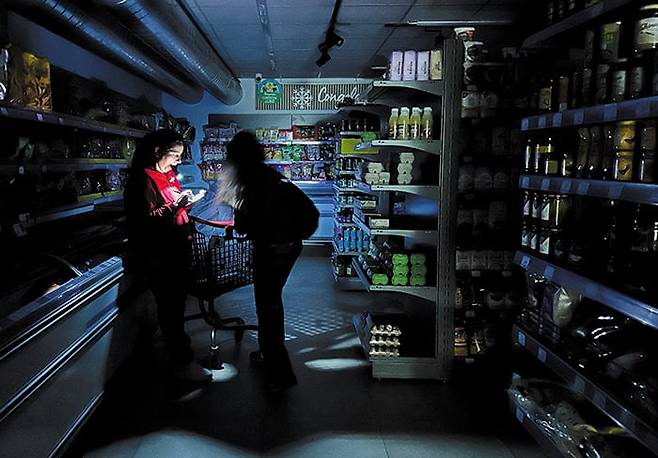 어둠 속의 쇼핑. 지난 28일 스페인·포르투갈 정전 사태로 일대 혼란이 발생한 가운데 스페인 바르셀로나의 한 마트 직원이 휴대폰 조명을 밝히고 손님의 물품 구매를 돕고 있다. 이날 스페인 마드리드를 비롯한 대부분 지역과 포르투갈 수도 리스본 등에서 발생한 정전 사태로 교통이 마비되거나 엘리베이터가 멈추는 상황이 발생했다. 전력은 다음 날 대부분 복구됐다. /로이터 연합뉴스