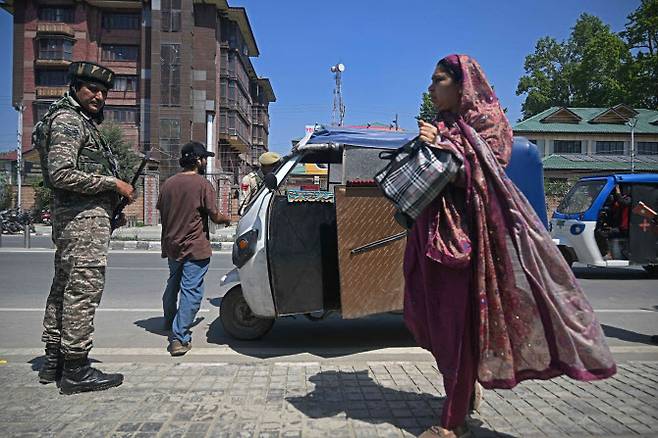 A commuter walks past an Indian paramilitary trooper, along a street in Srinagar on April 30, 2025. Indian Prime Minister Narendra Modi has given the military “operational freedom” to respond to a deadly attack in Kashmir that New Delhi has blamed on arch-rival Pakistan, a senior government source told AFP on April 29. (Photo by Tauseef MUSTAFA / AFP)