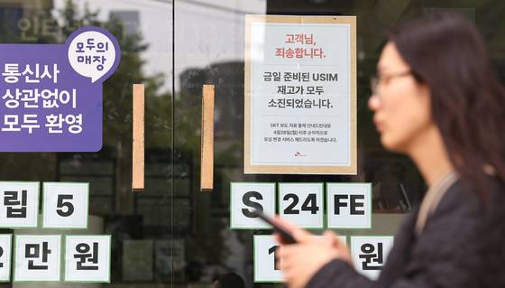 A woman walks past an SK Telecom store in Seoul on April 27, where a sign apologizes to customers for running out of SIM card replacements. [NEWS1]