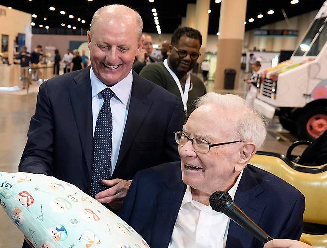 올해 말 은퇴 계획을 밝힌 워런 버핏 미국 버크셔해서웨이 회장(오른쪽)이 2일(현지 시간) 네브래스카주 오마하에서 열린 버크셔 주주총회의 자선 행사에서 상품으로 등장한 베개를 들고 있다. 그의 후임자인 그레그 에이블 버크셔 비(非)보험부문 부회장이 이를 보며 웃고 있다. 오마하=AP 뉴시스