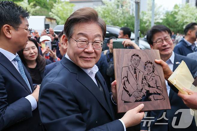 이재명 더불어민주당 대통령 후보가 2차 골목골목 경청투어에 나선 5일 오후 충북 진천군의 혁신도시 상가를 찾아 한 시민으로부터 이 후보와 김혜경 여사를 나무판에 각인한 그림판을 선물받고 있다. 2025.5.5/뉴스1 ⓒ News1 안은나 기자