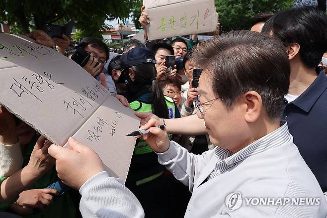 공판 연기 환영 팻말에 이재명 후보 '맞습니다' (전주=연합뉴스) 류영석 기자 = 더불어민주당 이재명 대선 후보가 '골목골목 경청투어:국토종주편'에 나선 7일 전북 전주시 풍남문 앞 광장에서 지지자들에게 인사를 하던 도중 한 지지자가 든 '공판 연기 환영, 대통령은 국민이 뽑습니다'라는 팻말에 사인을 하고 있다.
    이날 서울고등법원은 오는 15일 예정됐던 이 후보의 공직선거법 위반 혐의 사건 파기환송심 첫 공판을 오는 6월 18일로 연기했다. 2025.5.7 ondol@yna.co.kr