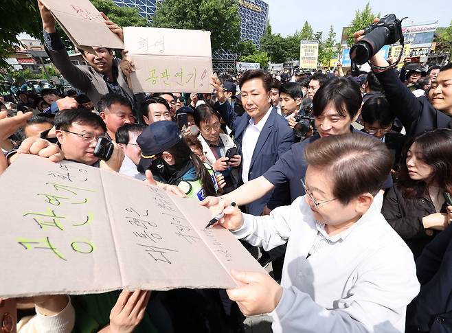 이재명 더불어민주당 대선후보가 7일 전북 전주시 완산구 풍남문 인근에서 공판연기를 환영하는 지지자의 응원 피켓에 사인을 해주고 있다. '공판연기 환영, 대통령은 국민이 뽑습니다'라고 적힌 피켓에 이 후보는 '맞습니다' 라고 썼다. /뉴시스