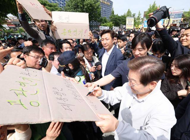 민심을 청취하는 '경청 투어'에 나선 이재명 더불어민주당 대선 후보가 7일 전북 전주시 완산구 풍남문 인근에서 공판 연기를 환영하는 지지자의 응원 피켓에 사인을 해주고 있다. '공판 연기 환영, 대통령은 국민이 뽑습니다'라고 적힌 피켓에 이 후보는 '맞습니다'라고 쓰고 있다. 전주=뉴시스