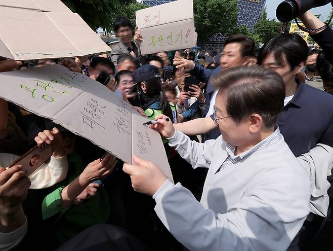 이재명 더불어민주당 대선후보가 5월7일 전북 전주시 풍남문 앞 광장에서 지지자가 든 '공판 연기 환영, 대통령은 국민이 뽑습니다'라는 팻말에 사인을 하고 있다. ⓒ연합뉴스