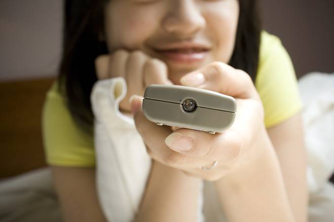 여자 청소년이 리모컨으로 조작하며 TV를 시청하고 있다. 포화지방과 설탕·소금 등이 많이 들어 있는 유해식품에 대한 광고를 5분만 봐도,  어린이·청소년은 하루에 약 130kcal의 열량을 더 섭취하는 것으로 나타났다.[사진=게티이미지뱅크]