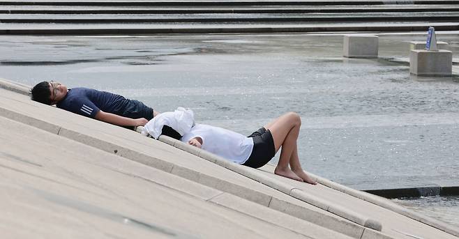 Two visitors at Yeouido Hangang Park sunbathe by a fountain on Tuesday, as daytime temperatures ranged bewteen 20 to 29 degrees Celsius that day. (Yonhap)