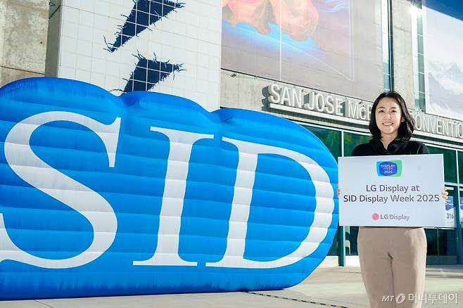 LG디스플레이 직원이 12일(현지시간) 세계 최대 디스플레이 전시회 'SID 2025'가 열리는 미국 새너제이 맥에너리컨벤션센터 앞에서 참가 소식을 알리고 있다./사진=LG디스플레이