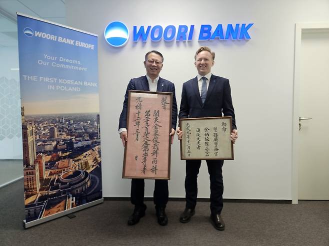 정진완(왼쪽) 우리은행장이 지난 7일(현지시간) 폴란드 바르샤바 우리은행 폴란드지점에서 마테우슈 오르딕 부지점장과 기념촬영을 하고 있다. 마테우슈 부지점장의 외고조부인 김병준 씨의 1886년 무과급제 교지와 1897년 정3품 통정대부 칙명(임명장)을 정 행장과 마테우슈 부지점장이 각각 들고 있다.  [우리은행 제공]