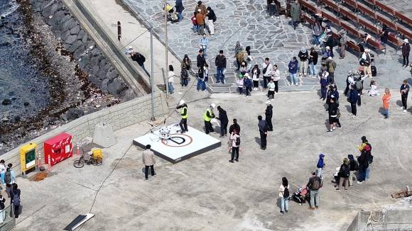 지난 10일부터 올해 첫 비양도 드론배송서비스를 실시하는 기념으로 비양리 마을회에서 쿠키 등 간식을 마련해 한림읍 금능해변에서 비양도까지 드론배송을 실시하고 있다. 사진은 비양도로 배달된 간식을 주민들과 탐조대회에 참가한 학부모와 아이들이 바라보고 있는 모습. 제주도 제공