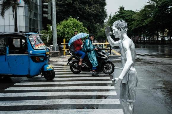 지난달 1일 인도네시아 자카르타의 한 도로에서 온몸을 은색 페인트로 칠한 아리 무난다르가 비를 맞으며 로봇 자세를 취하고 있다. AFP 연합뉴스