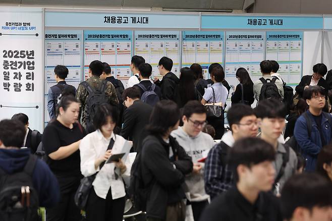 지난 21일 서울 강남구 코엑스에서 열린 2025 중견기업 일자리 박람회를 찾은 구직자들이 채용공고 게시물을 보고 있다. [연합]