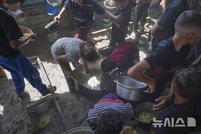 [칸유니스=AP/뉴시스] 9일(현지 시간) 가자지구 남부 칸유니스에서 음식 배급이 끝난 뒤 팔레스타인 어린이들이 배급 용기에 남은 음식을 긁어모으고 있다. 2025.05.10.