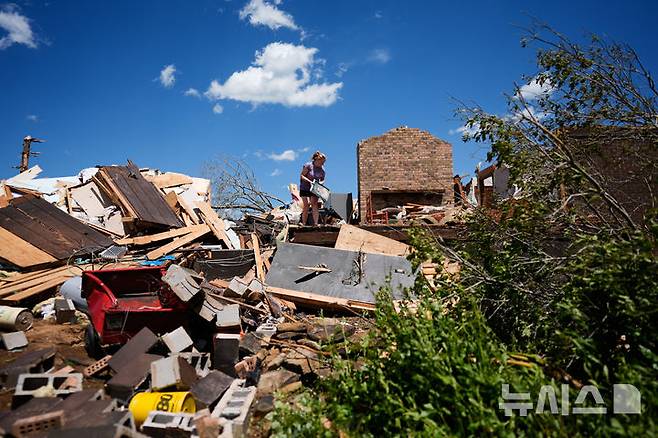 [런던( 미 켄터키주)=AP/뉴시스] 미 켄터키주의 주민 헤일리 앨런이 토네이도로 완파된 집터에서 5월 17일 가족 사진을 가까스로 구해내 옮기고 있다. 2025. 05. 18.