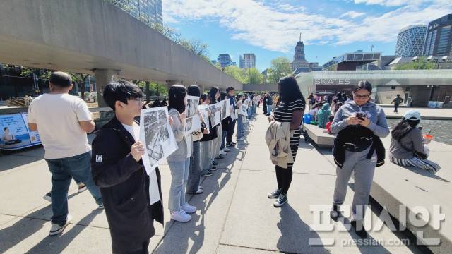▲'책으로 세계'로 프로그램에 참여한 광주 학생 20여명이 캐나다 토론토 중심가 네이선필립스광장에서 5·18민주화 운동 당시의 사진과 설명이 담긴 용지를 들고 있다.ⓒ광주시교육청