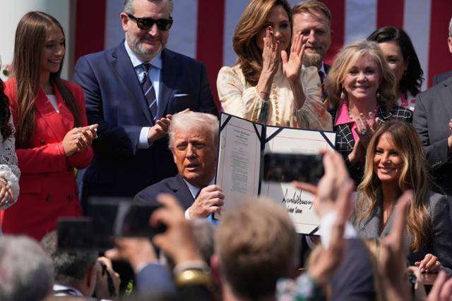 도널드 트럼프(가운데) 미국 대통령이 19일 워싱턴 백악관 로즈가든에서 영부인 멜라니아 여사와 자신이 서명을 마친 테이크 잇 다운 법을 들어 보이고 있다. 워싱턴=AP 연합뉴스