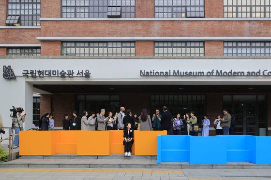 국립현대미술관 서울 주출입구를 가로막은 색색의 긴 의자는 전시 '기울인 몸들: 서로의 취약함이 만날 때' 출품작이다. 15일 언론공개회 참석자들이 작품을 살펴보고 있다. 수어 사용자들도 마주 앉아 대화할 수 있는 구조다. 연합뉴스