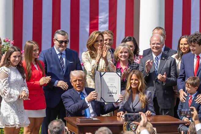 도널드 트럼프 미국 대통령이 19일(현지시간) 백악관 로즈가든에서 열린 리벤지 포르노 처벌 법안 서명식에서 아내 멜라니아 여사와 함께 법안에 서명한 뒤 법안을 들어보이고 있다. 연합뉴스