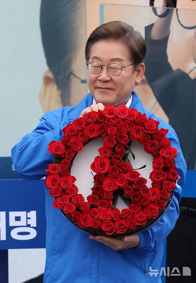 [고양=뉴시스] 조성우 기자 = 이재명 더불어민주당 대선후보가 20일 경기 고양시 일산동구 일산문화광장 앞에서 열린 집중유세에서 장미로 만든 투표기호 화환을 선물받고 있다. 2025.05.20. xconfind@newsis.com