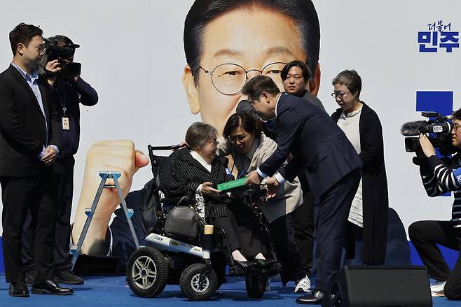 장애인권운동가 박김영희 장애인차별금지추진연대 상임대표(휠체어 탄 이)가 2025년 5월12일 서울 광화문 청계광장에서 이재명 더불어민주당 대선 후보에게 국민의 질문을 모은 ‘모두의질문큐(Q)’ 녹서를 전달하고 있다. 연합뉴스