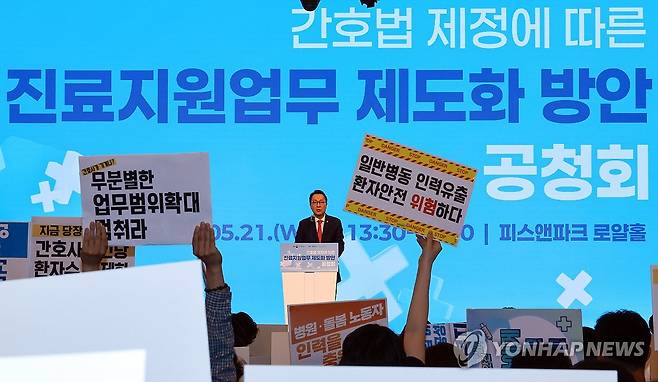 박민수 보건복지부 2차관 개회사 (서울=연합뉴스) 신현우 기자 = 박민수 보건복지부 제2차관이 21일 서울 용산구 피크앤파크 컨벤션 로얄홀에서 열린 간호법 제정에 따른 진료지원업무 제도화 방안 공청회에 참석해 개회사를 하는 가운데 전국민주노동조합총연맹 공공운수노조 의료연대본부 조합원이 피케팅하고 있다. 2025.5.21 nowwego@yna.co.kr