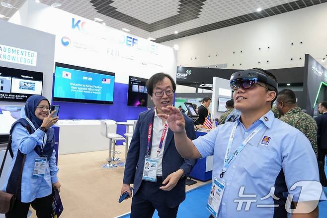 지난 21일(현지시간) 말레이시아 방산전시회 'LIMA 2025'에 마련된 한국관에서 조근식 증강지능 대표(가운데)가 인공지능(AI) 기반 혼합현실(MR)을 이용한 항공 정비 시뮬레이터 체험을 안내하고 있다. (한국방위산업진흥회 제공. 재판매 및 DB 금지) 2025.5.22/뉴스1