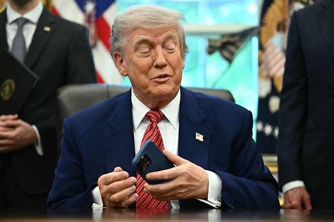 도널드 트럼프 미국 대통령이 23일(현지시각) 백악관 집무실에서 기자들과 만나 이야기를 나누던 중 자신의 스마트폰을 만지고 있다. /AFP 연합뉴스