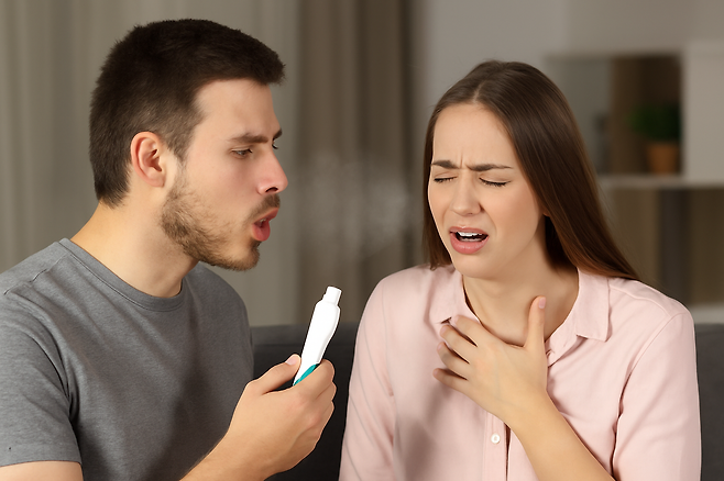 치약을 손에쥐고 입김을 부는 남성과 목에 손을 얹고 괴로워하는 여성