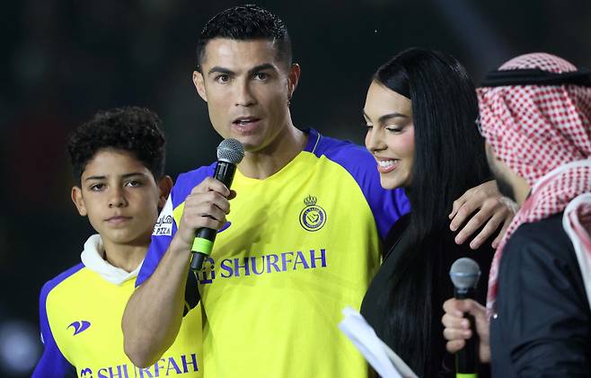 <yonhap photo-4333=""> (FILES) Portuguese forward Cristiano Ronaldo (C-L), accompanied by his partner Georgina Rodriguez (C-R) and his son Cristiano Ronaldo Jr (L), greets the crowd at the Mrsool Park Stadium in the Saudi capital Riyadh on January 3, 2023, upon his presentation as an Al-Nassr player. Cristiano dos Santos, the eldest son of five-time Ballon d'Or winner Cristiano Ronaldo, was called up to the Portugal Under-15 squad for the first time on May 6, 2025. The 14-year-old, who, like his father, plays for Al-Nassr in Saudi Arabia, has also had spells with Ronaldo's former clubs Manchester United and Juventus. (Photo by FAYEZ NURELDINE / AFP)/2025-05-06 21:47:08/ <저작권자 ⓒ 1980-2025 ㈜연합뉴스. 무단 전재 재배포 금지, AI 학습 및 활용 금지></yonhap>