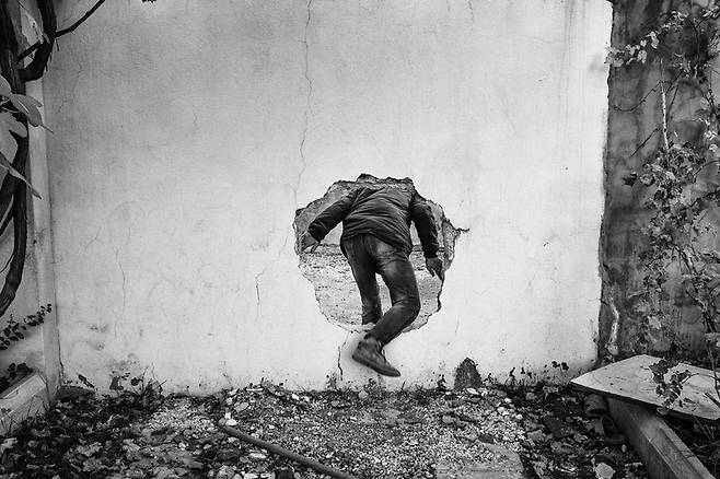 A member of Civilian Protection Unit (YPS) uses a hole in a wall to cross a street controlled by Turkish special military forces, Nusaybin, Turkey, December 2015(C) Emin Ozmen/Magnum Photos