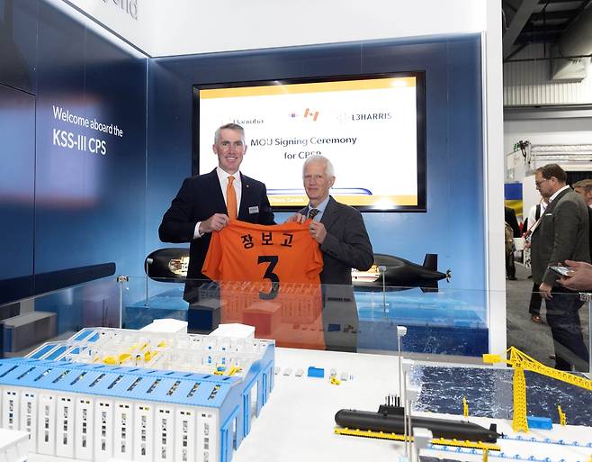 Hanwha Global Defense CEO Michael Coulter (left) and Rich Foster, vice president of L3Harris Technologies Canada, pose after signing a partnership at CANSEC 2025, holding a uniform with the name “JangBogo 3,” representing the KSS-III-class submarines. (Hanwha Ocean)